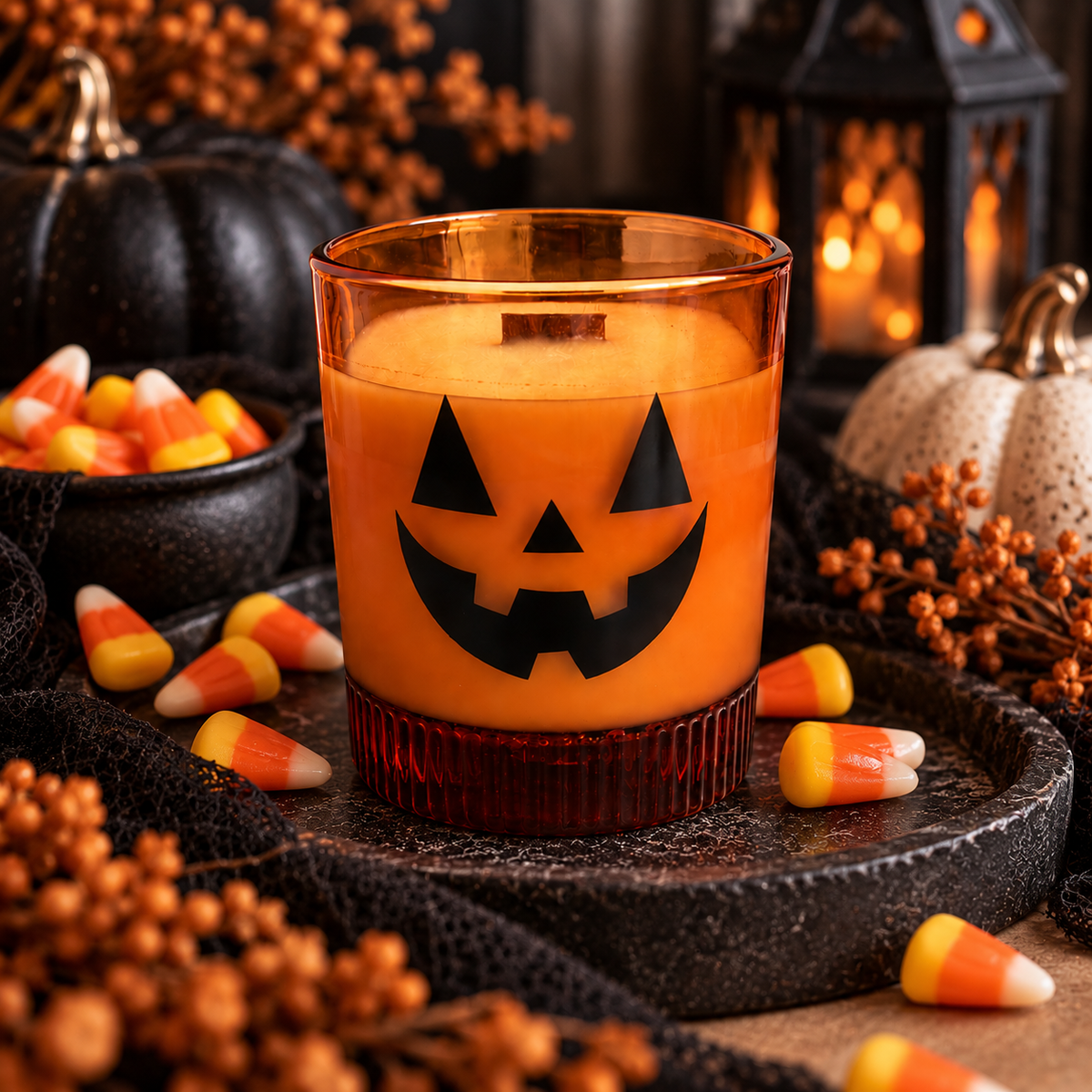Orange jack-o'-lantern glass soy candle beside candy corn in a Halloween display